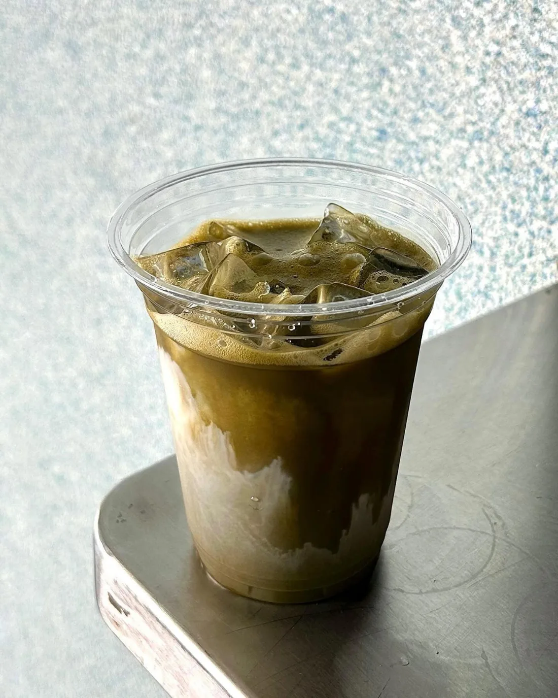 cornershop's iced dirty matcha in a clear cup, kopi poured over whisked matcha and milk, on the stall's stainless ledge