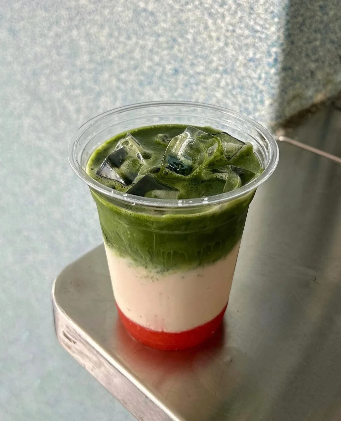cornershop's strawberry matcha in a clear cup on the stall's stainless ledge, deep red compote at the bottom, milk in the middle, whisked matcha on top